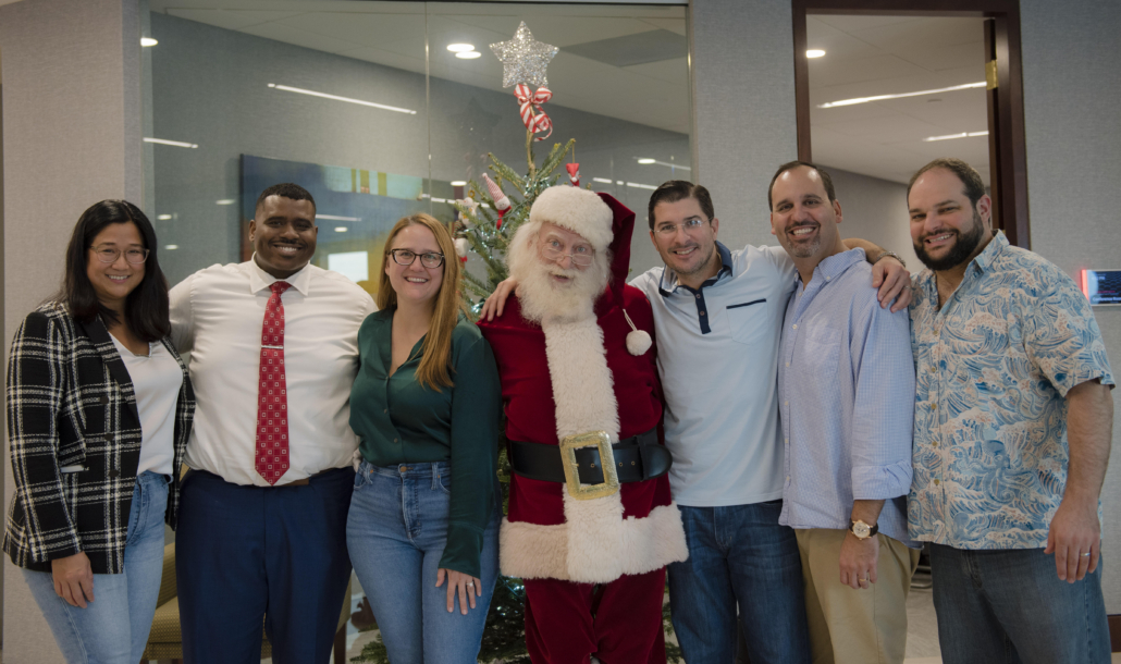A photo with members of the KTT Law team with Santa Claus at a holiday party in 2023. From left to right: Bernice C. Lee, Dwayne A. Robinson, Maria D. Garcia, Santa, Javier A. Lopez, Tal J. Lifshitz, and Benjamin J. Widlanski